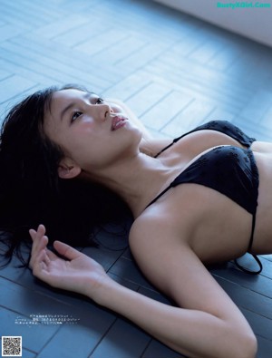 A woman in a blue bikini sitting on a towel by a pool.