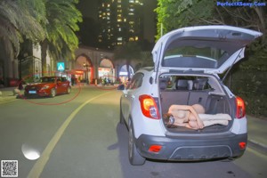 A naked woman wearing a face mask standing next to a car.