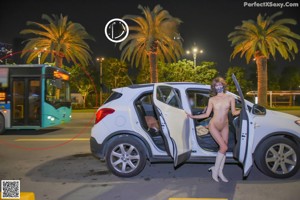 A naked woman wearing a face mask standing next to a car.