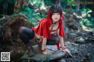A woman in a red hooded outfit posing in the woods.