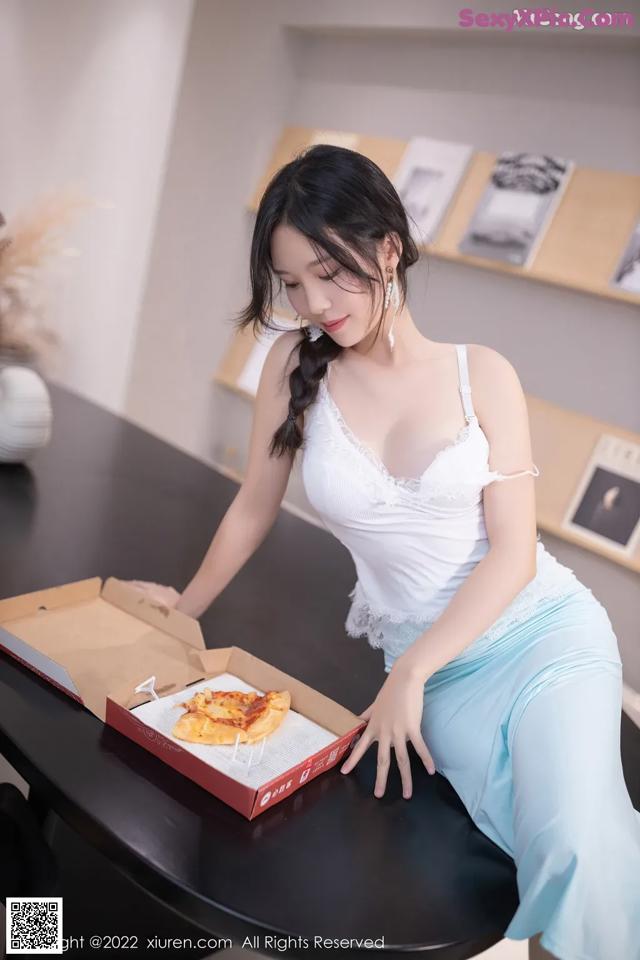 A woman sitting at a table with a pizza in a box.