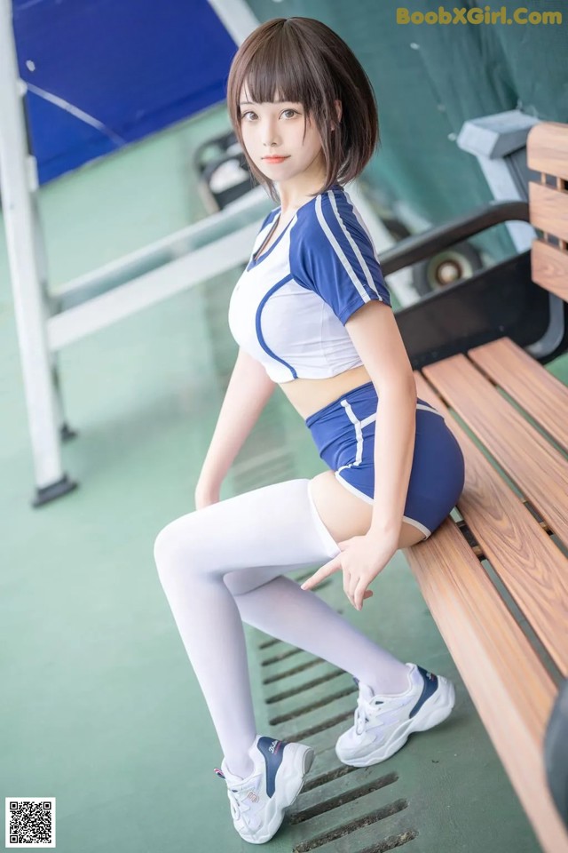 A woman sitting on a bench in a blue and white outfit.