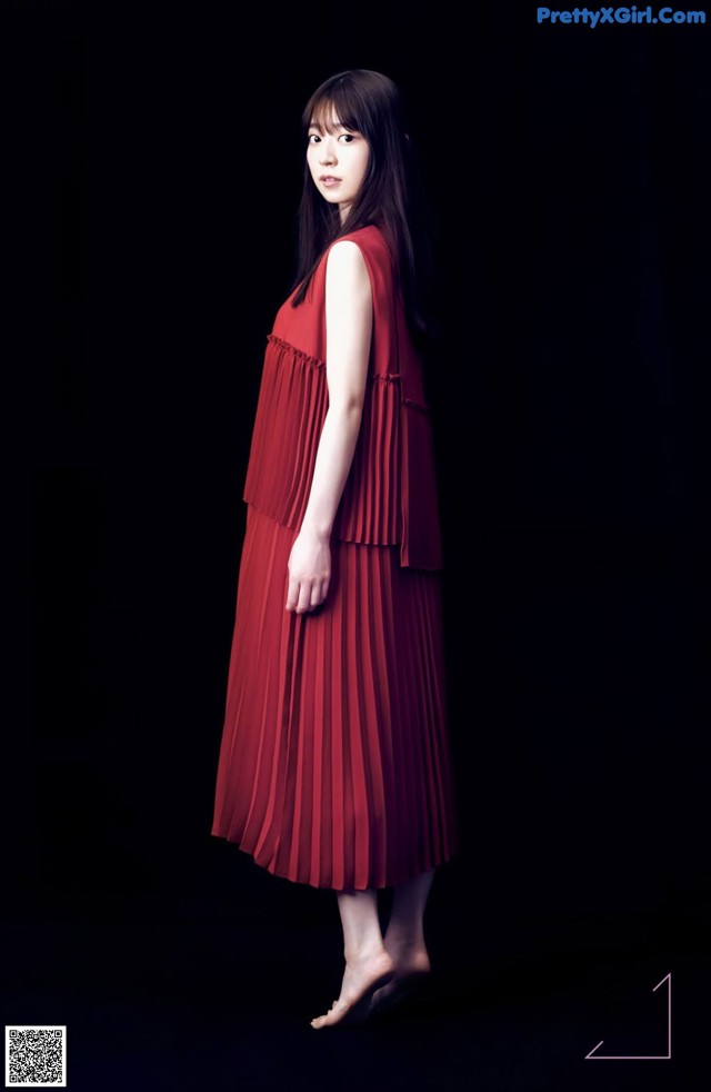 A woman in a red dress standing in front of a black background.