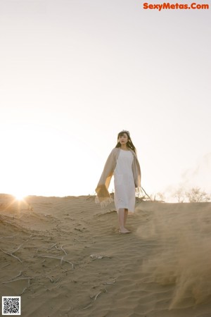 A woman in a white dress standing in the sand.