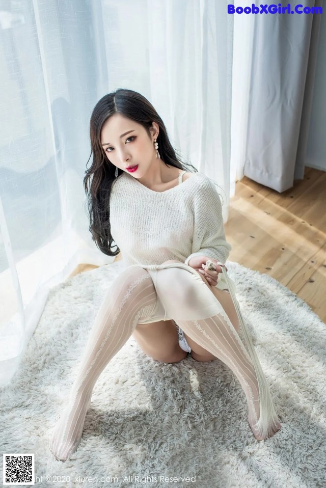 A woman in a white sweater and stockings sitting on a white rug.