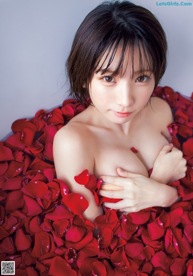 A woman laying in a bed of red rose petals.