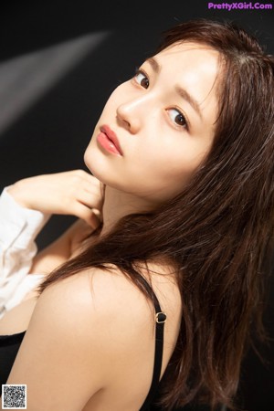 A woman in a black bra and white shirt leaning against a wall.