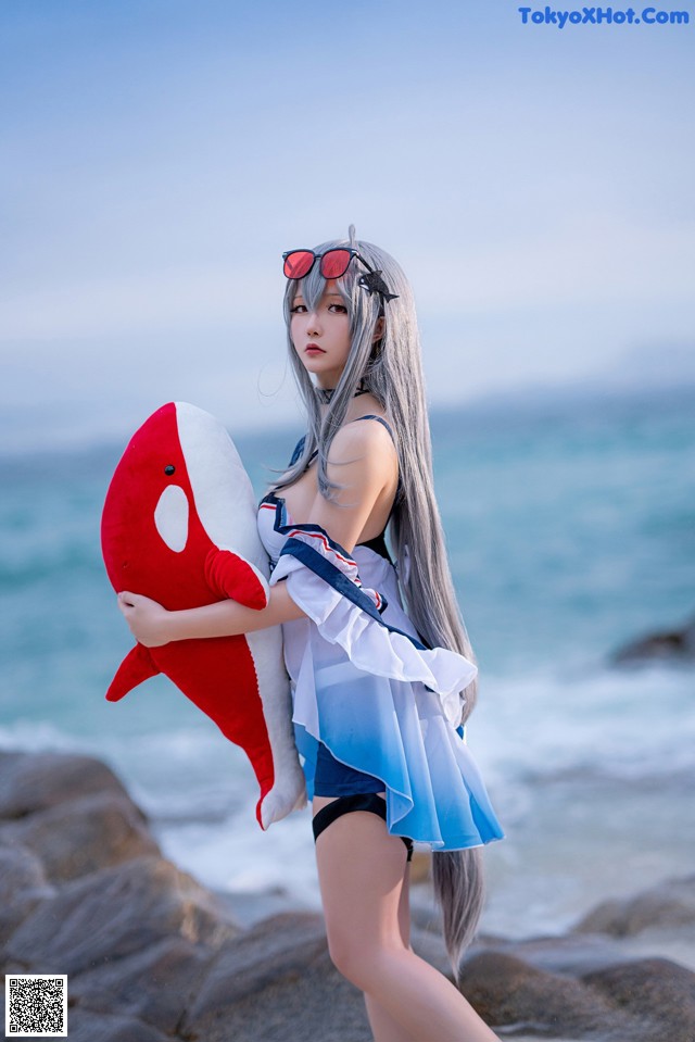 A woman in a bikini holding a stuffed shark on the beach.