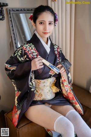 A woman in a black kimono sitting on a couch holding a fan.