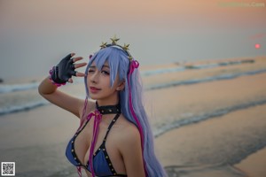 A woman with long blue hair is posing on the beach.