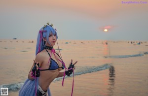 A woman with long blue hair is posing on the beach.