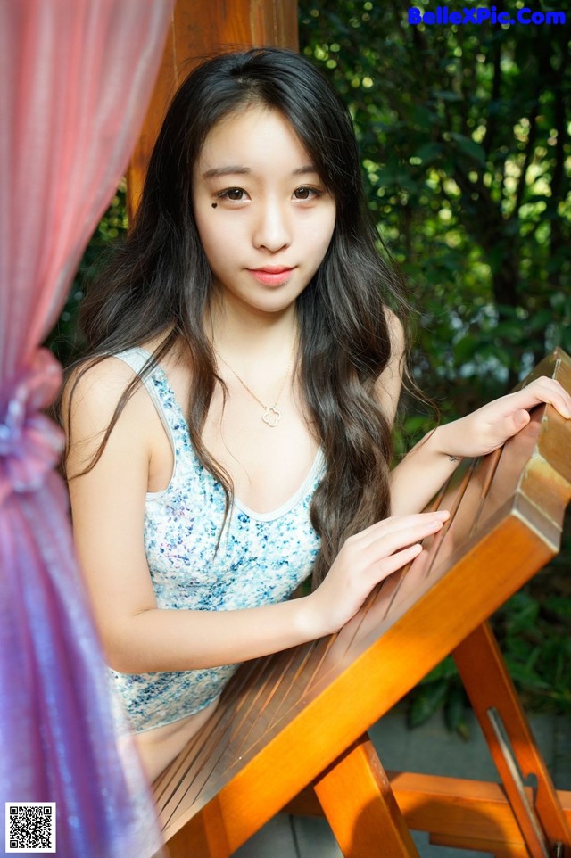 A young woman sitting on a wooden chair in a garden.