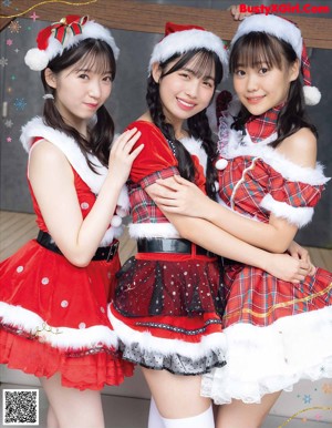 A couple of women dressed in santa claus outfits sitting on a fireplace.