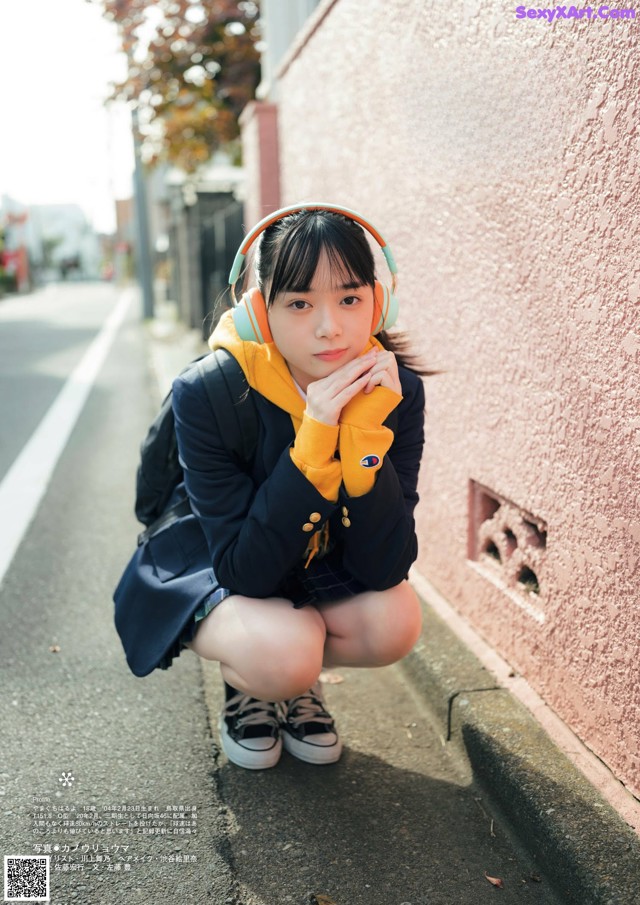 A young woman wearing headphones crouching down on the street.