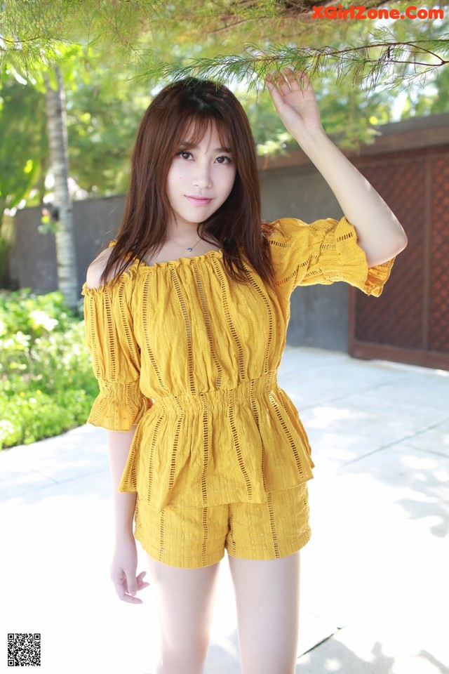 A woman in a yellow top and shorts posing for a picture.