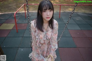 A woman sitting on a red swing in a park.