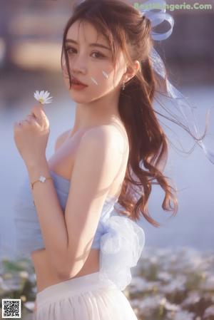 A woman in a blue top and white skirt holding a flower.