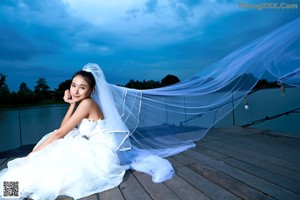 A woman in a wedding dress laying on a wooden dock.